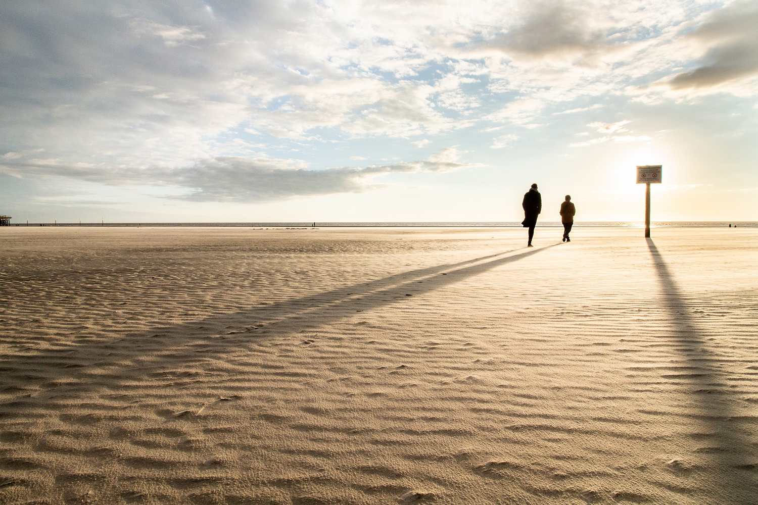 Zwei Menschen, die in der Ferne an einem Strand spazieren.
